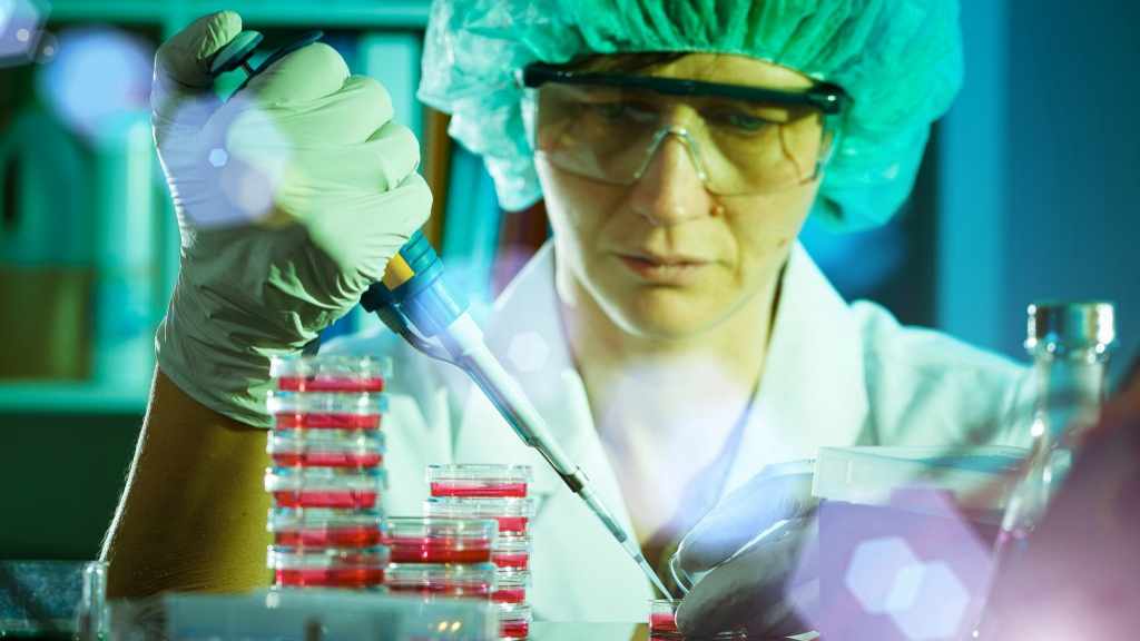 Acercamiento de un empleado que trabaja en investigación con los equipos del laboratorio, usando guantes y otras protecciones