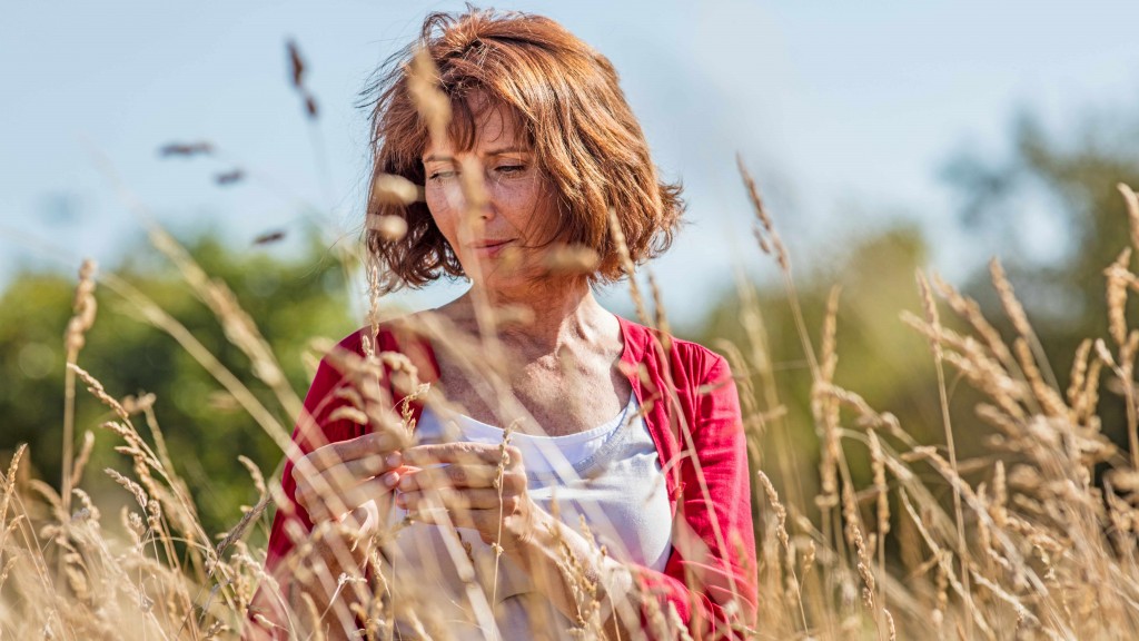 a middle-aged woman outside in a field, looking serious and thinking