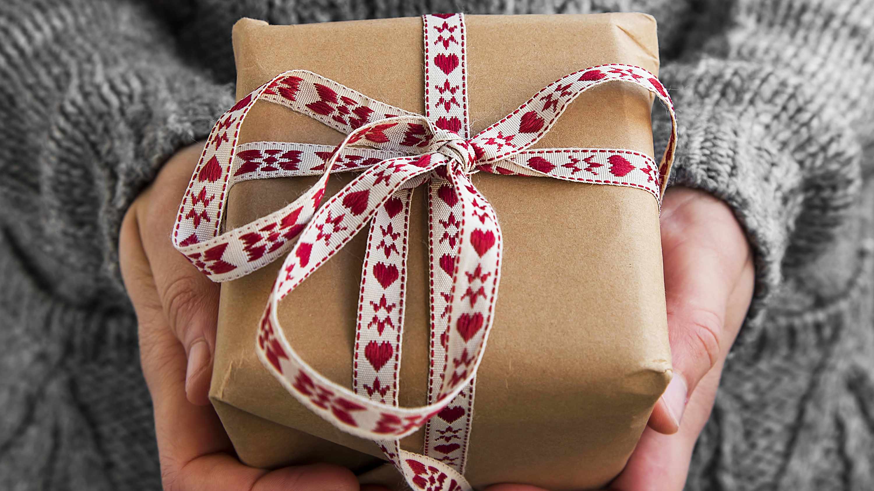 a person holding a present wrapped in brown gift paper with a heart ribbon