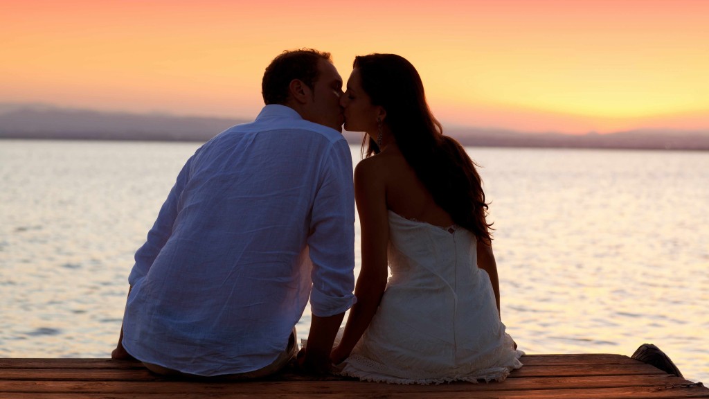 a young man and woman, couple sitting on boat dock kissing with sunset in background