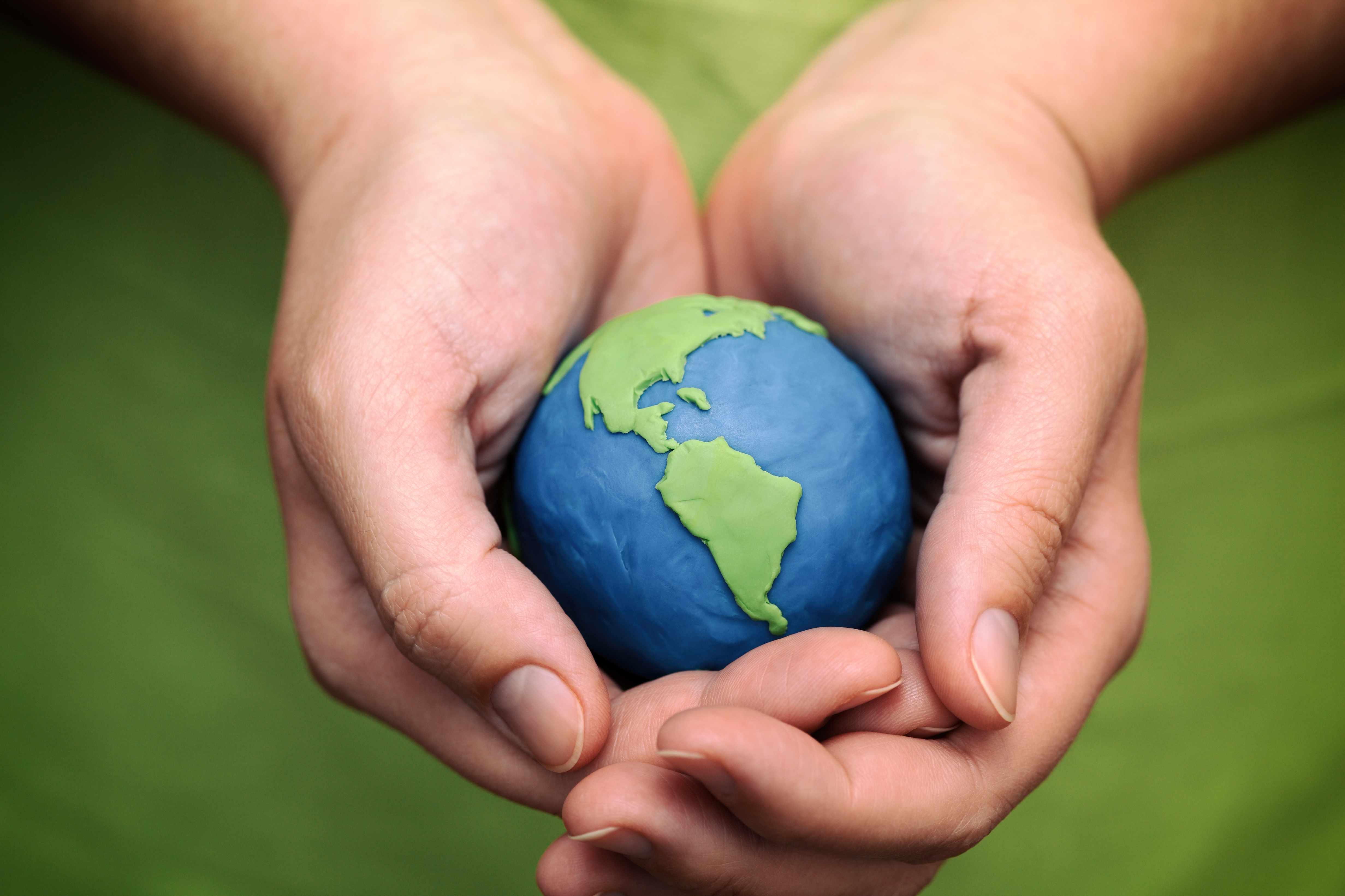 two hands holding a clay model of the earth, the world, a globe