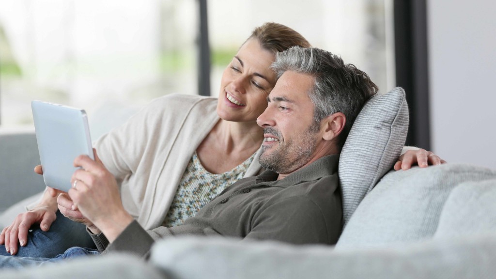 a middle-aged couple with gray hair sitting on a couch looking at a computer tablet
