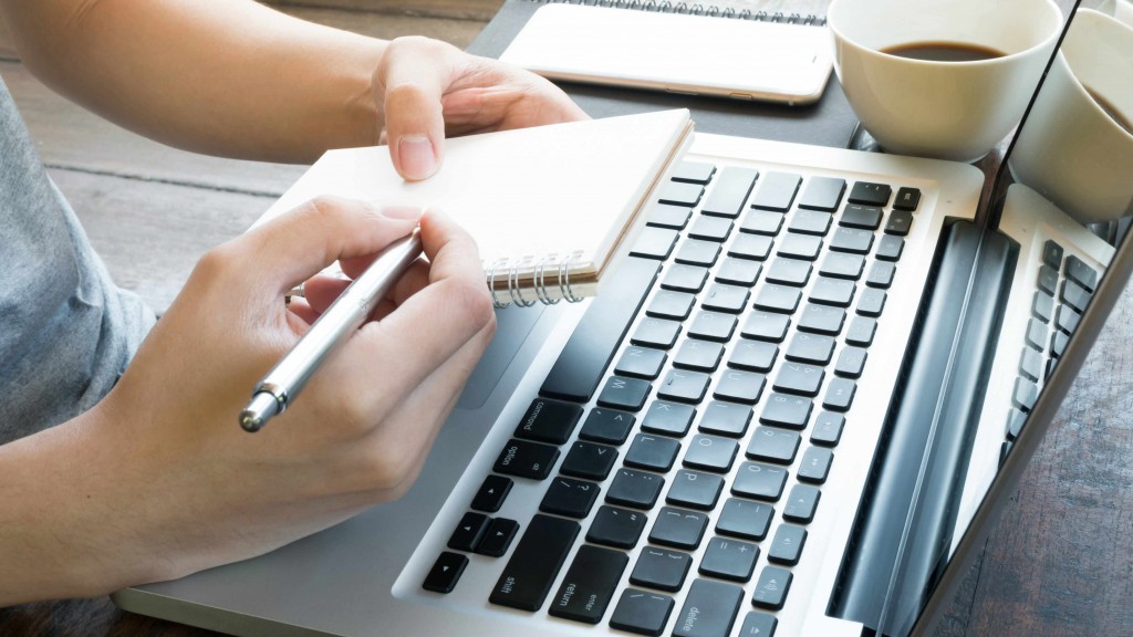 Una persona trabaja con una computadora portátil y usa papel y lápiz para tomar notas