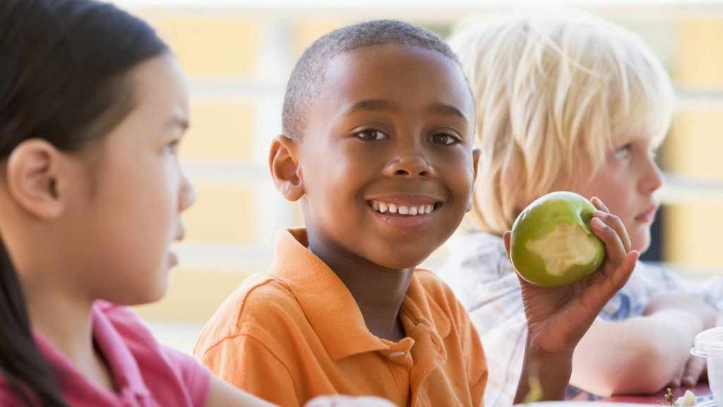 children at school lunch table, African-America boy eating an apple