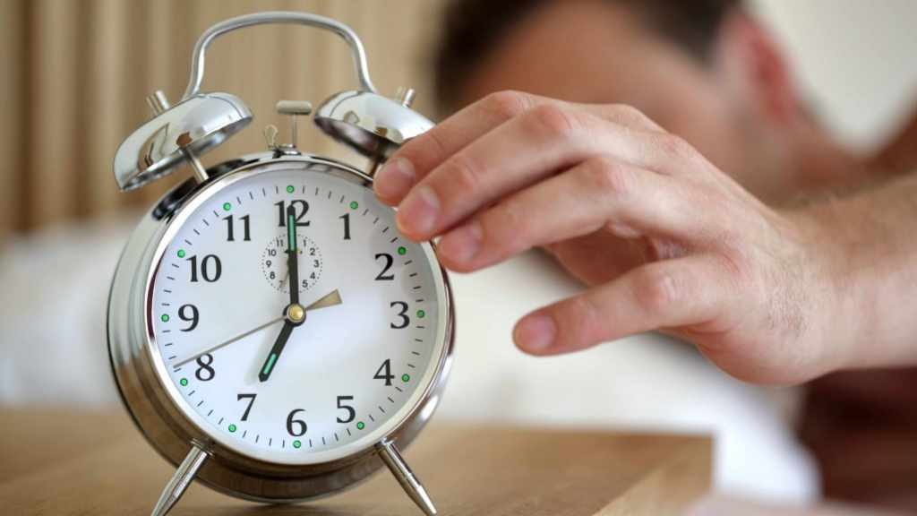 man waking up from sleep and turning off alarm clock