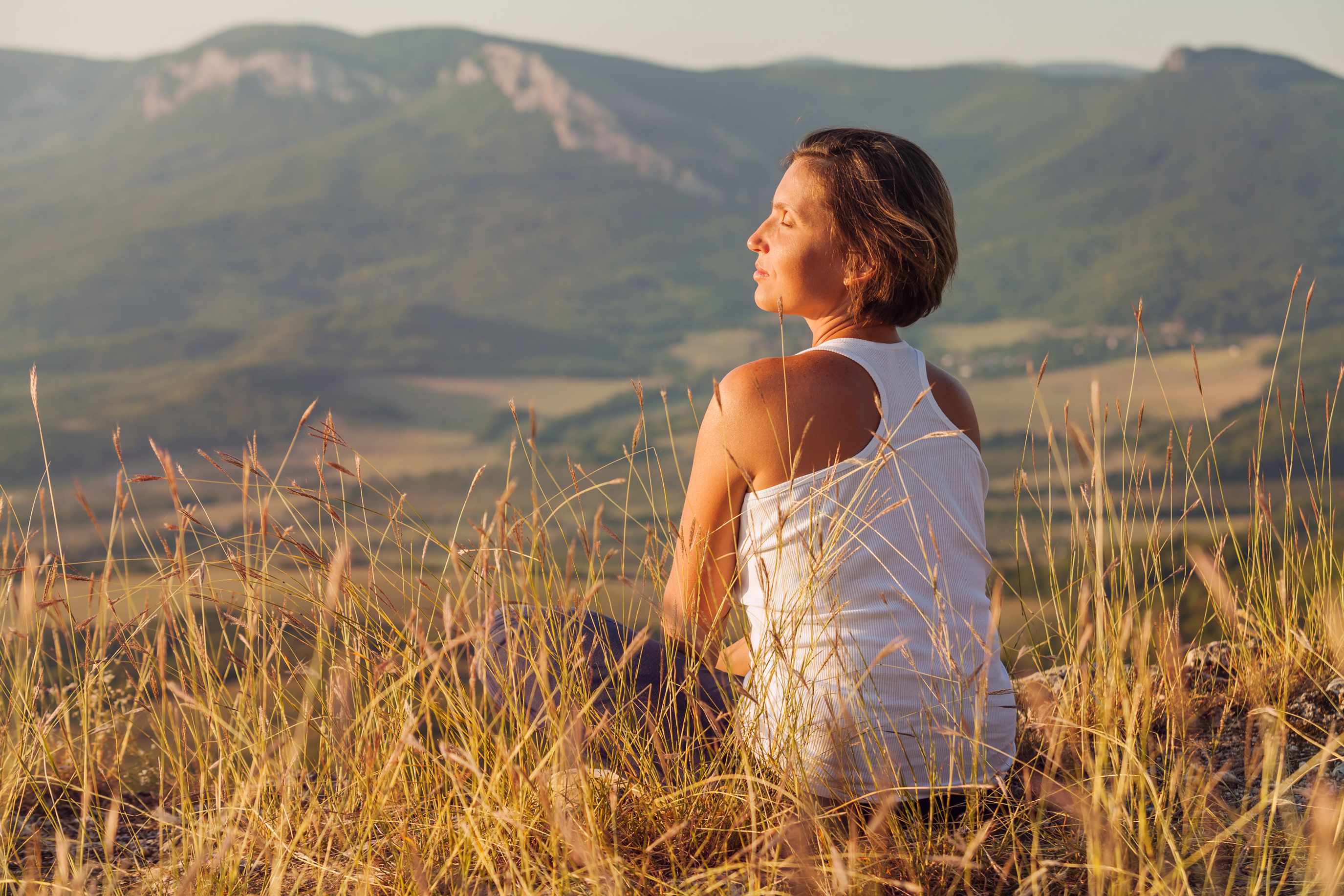 a woman sitting outside in a field enjoying the sunrise