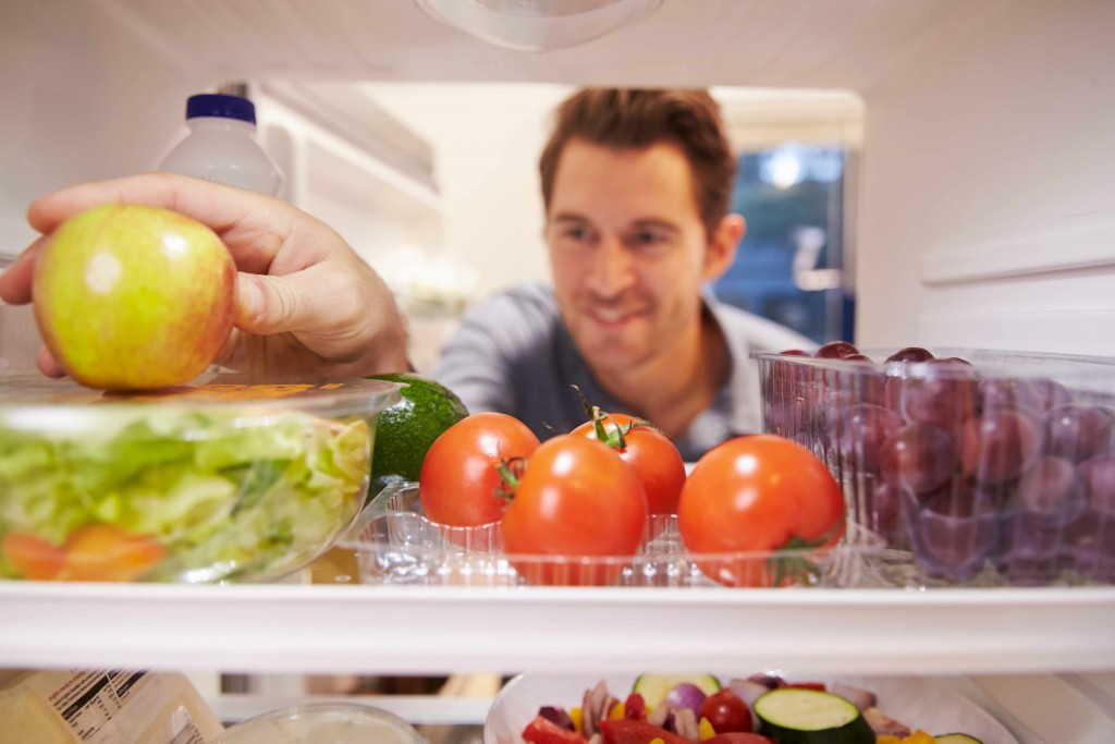 a man opening a refrigerator door with fruits and vegetables on the shelf