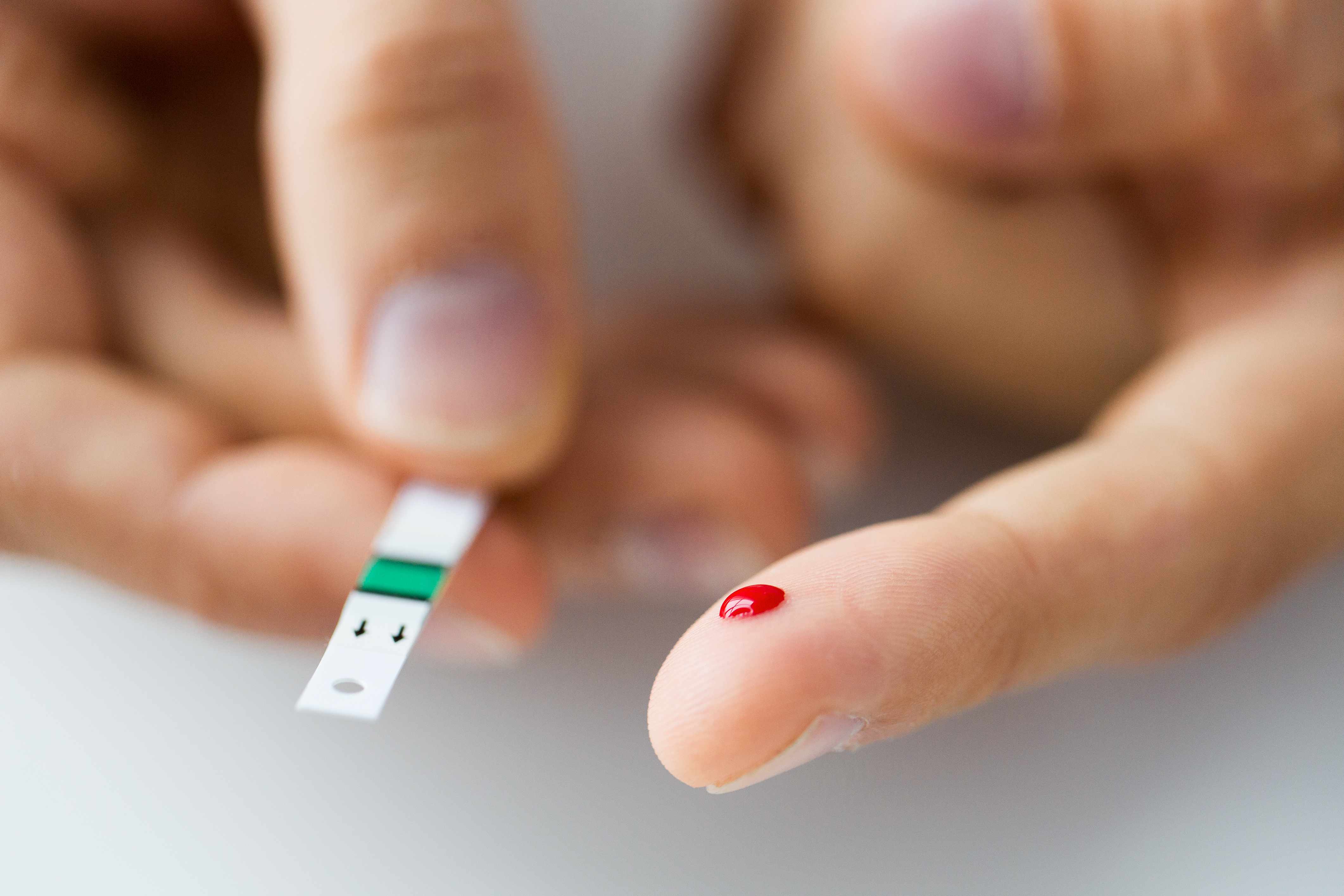 Acercamiento de un dedo masculino que gotea sangre sobre una tira reactiva para la prueba de la diabetes