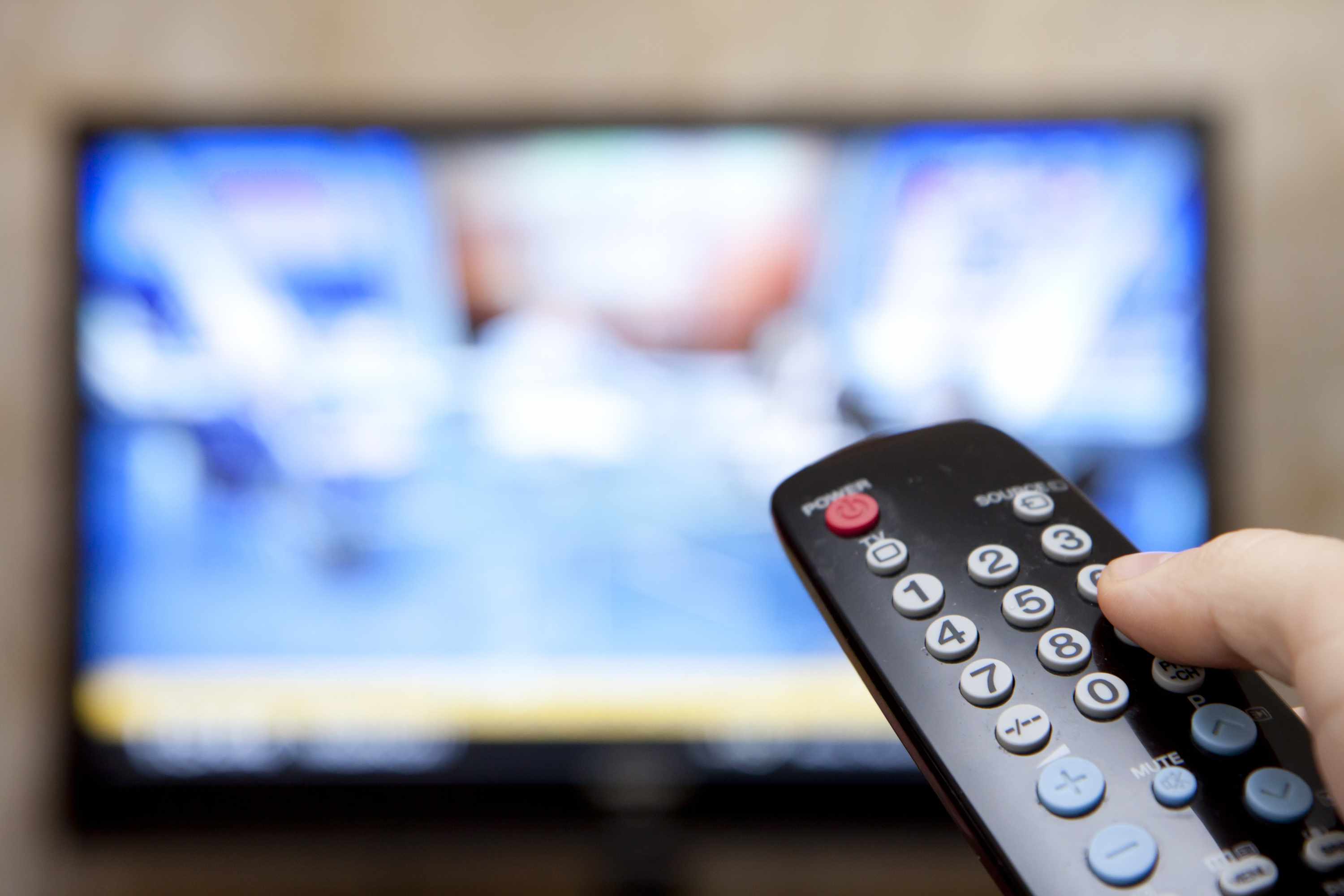 a person holding a television remote control with the TV blurred out in the background