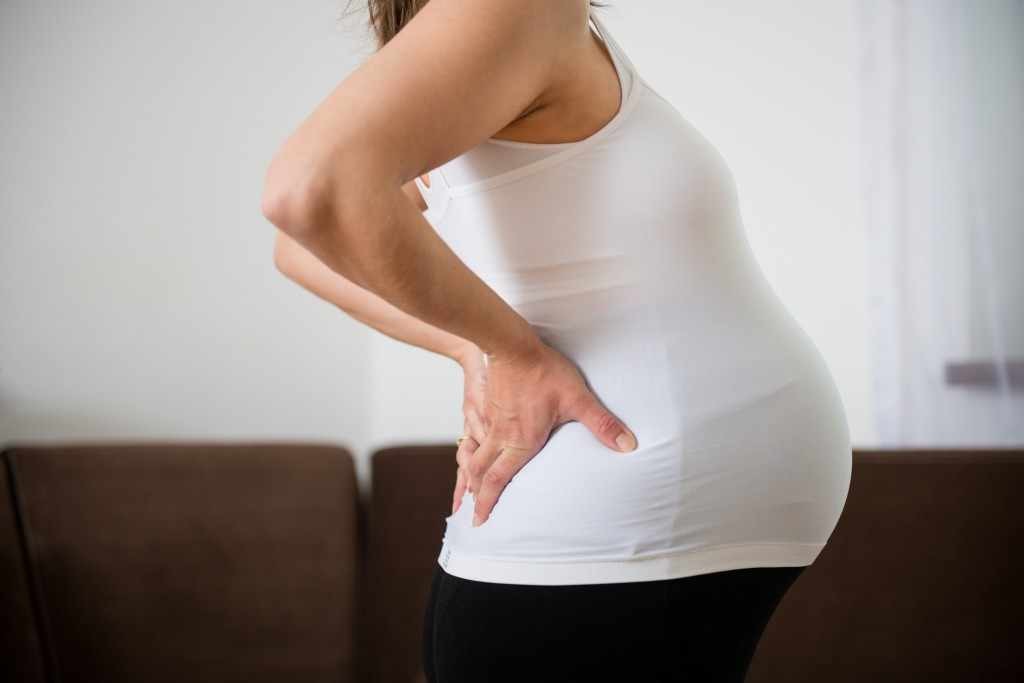 torso of pregnant woman in a exercise shirt holding her back
