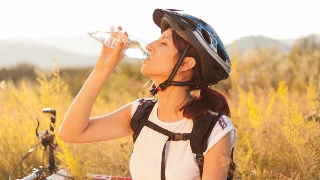 Una mujer anda en bicicleta y bebe agua de una botella