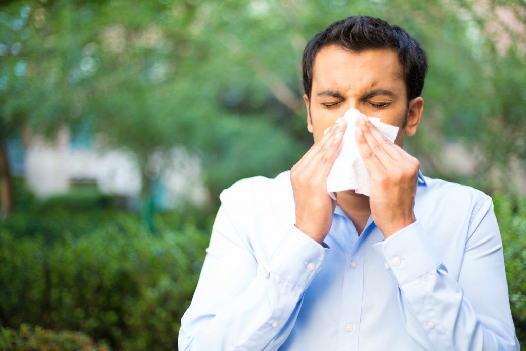 a man outside, blowing his nose, suffering from allergies