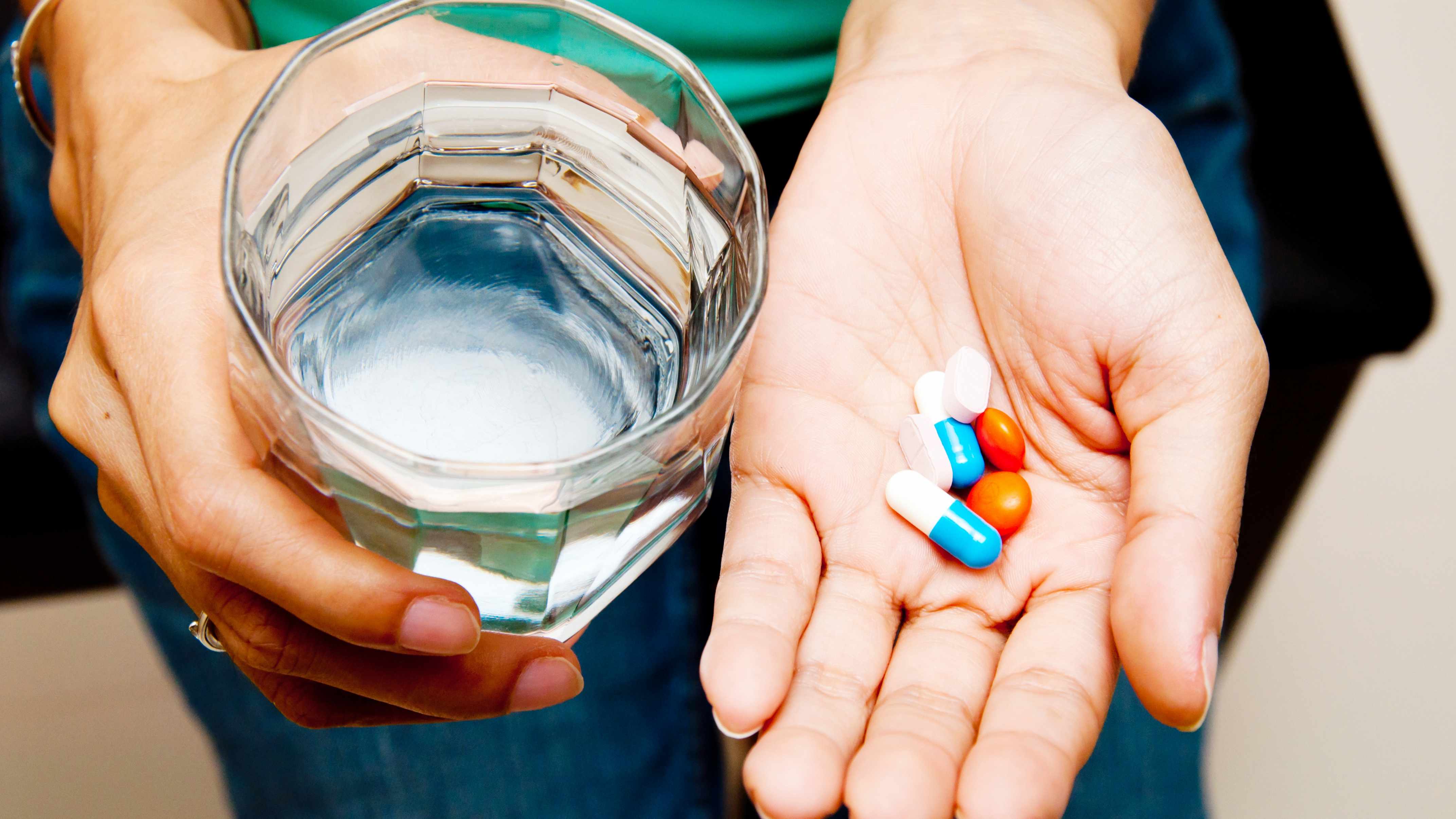 a person holding a glass of water and a handful of medication pills