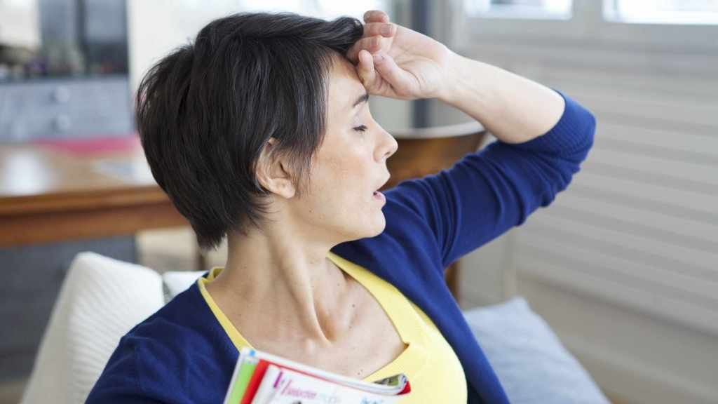 a woman holding her hand to her forehead, suffering from hot flashes caused by menopause