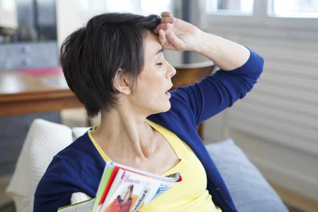 a woman holding her hand to her forehead, suffering from hot flashes caused by menopause