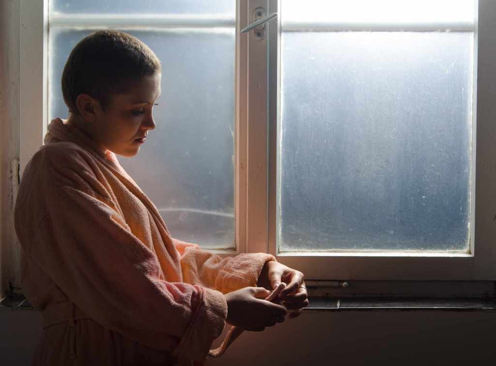 a cancer patient standing quietly by a window, looking pensive 