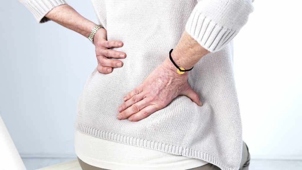 mujer mayor sostiene su espalda baja, sufriendo de dolor lumbar