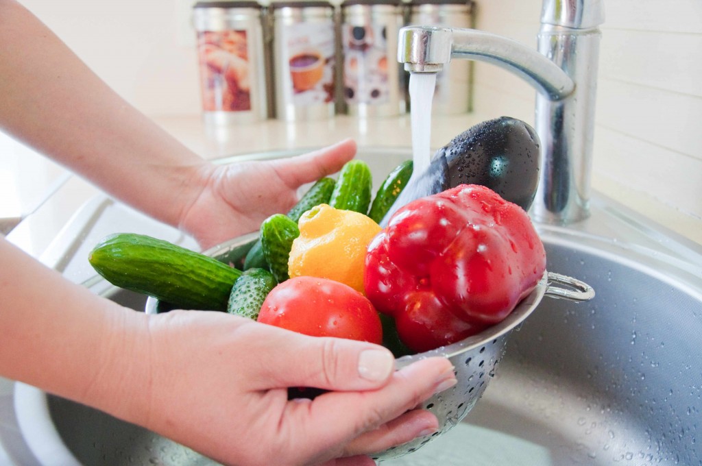 a person washing vegetables and fruits under kitchen water faucet