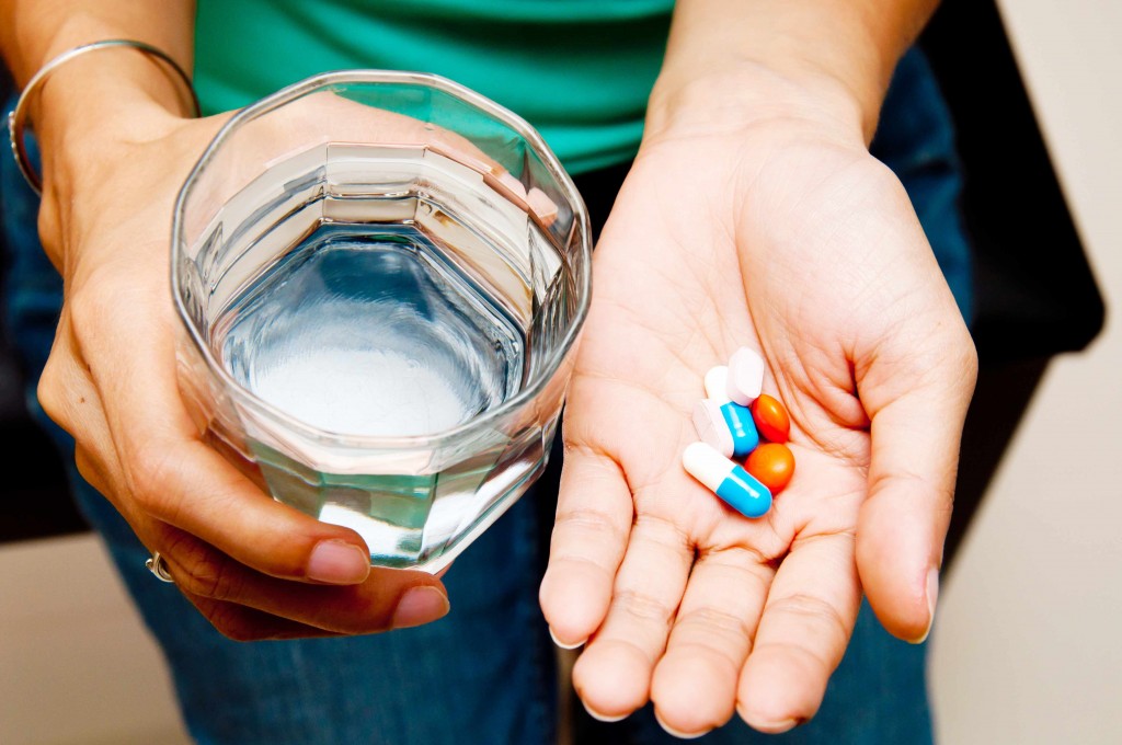 a person holding a glass of water and a handful of medication pills