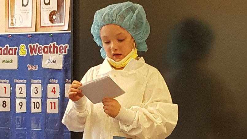 first-grader Olivia Worlton, in scrubs, giving her class presentation about her hero, Dr. Shaughnessy