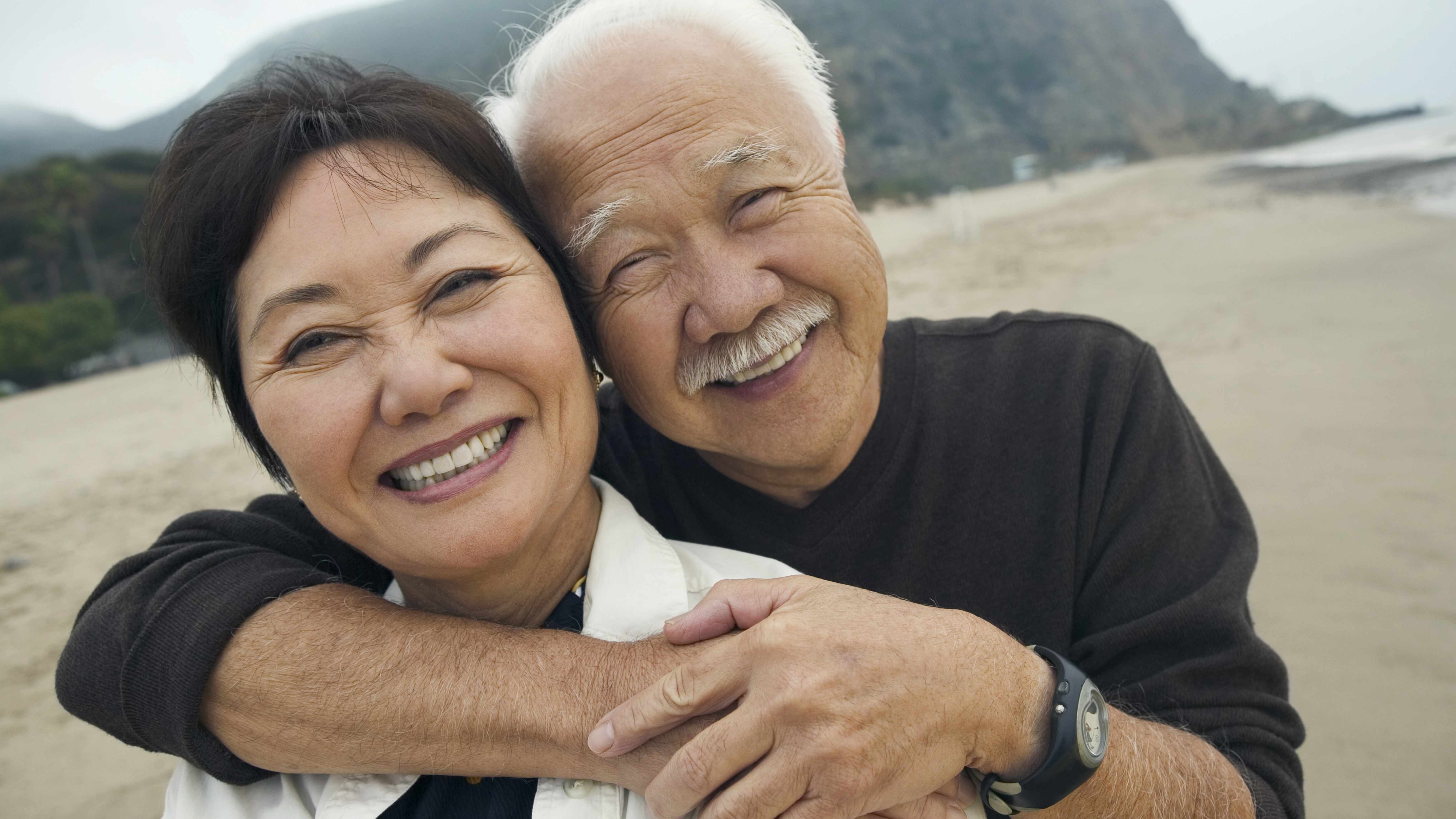 Un hombre y una mujer de mediana edad sonreídos y abrazados en la playa