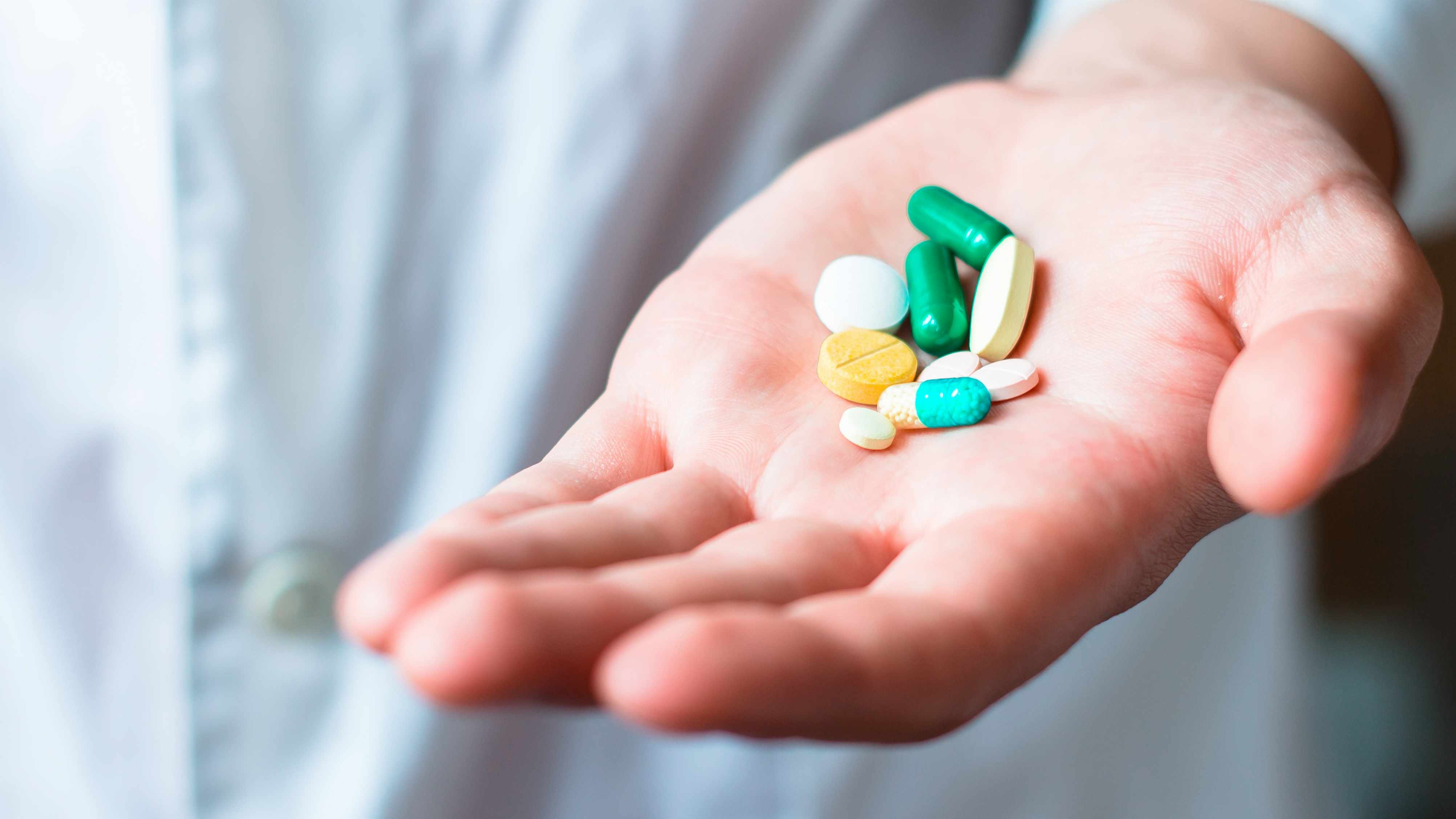 a person's hand full of medicine pills, prescription tablets, vitamins