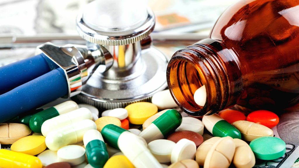 a pill bottle spilling prescription medicine, antibiotics, with a stethoscope nearby