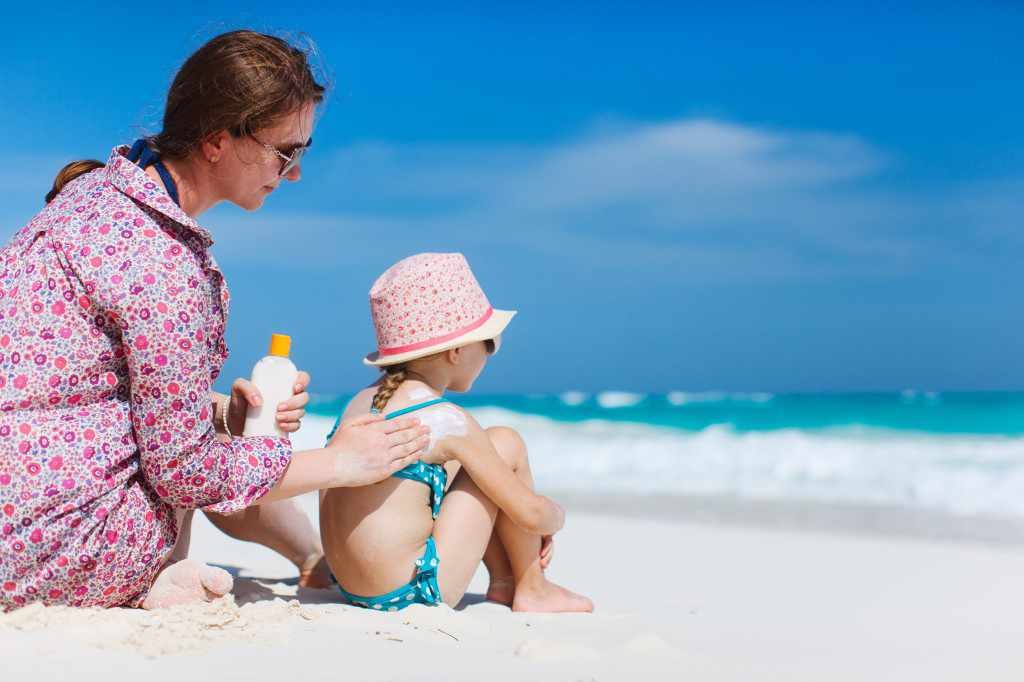 a mother applies sunscreen to a young child on the beach
