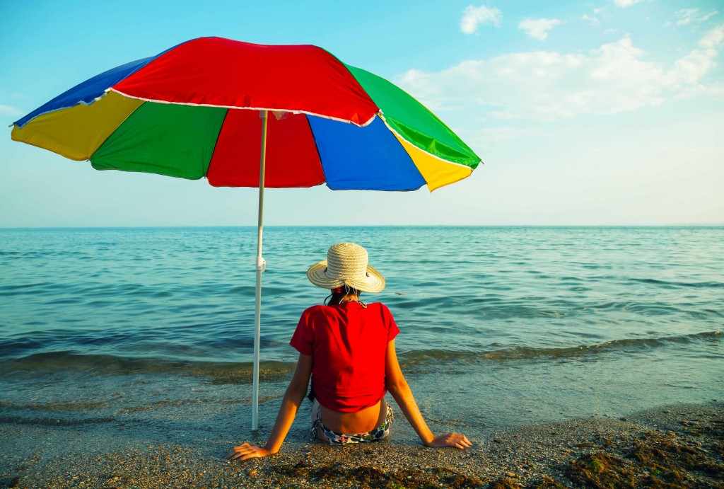 person sitting on the beach in a hat under the shade of an umbrella