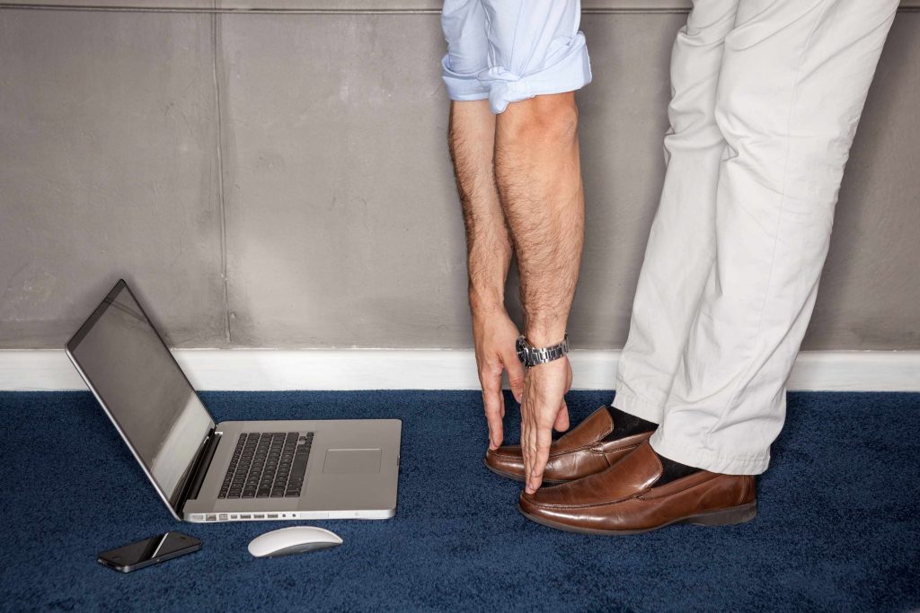 a man standing in his office doing exercises with laptop on floor, touching his toes