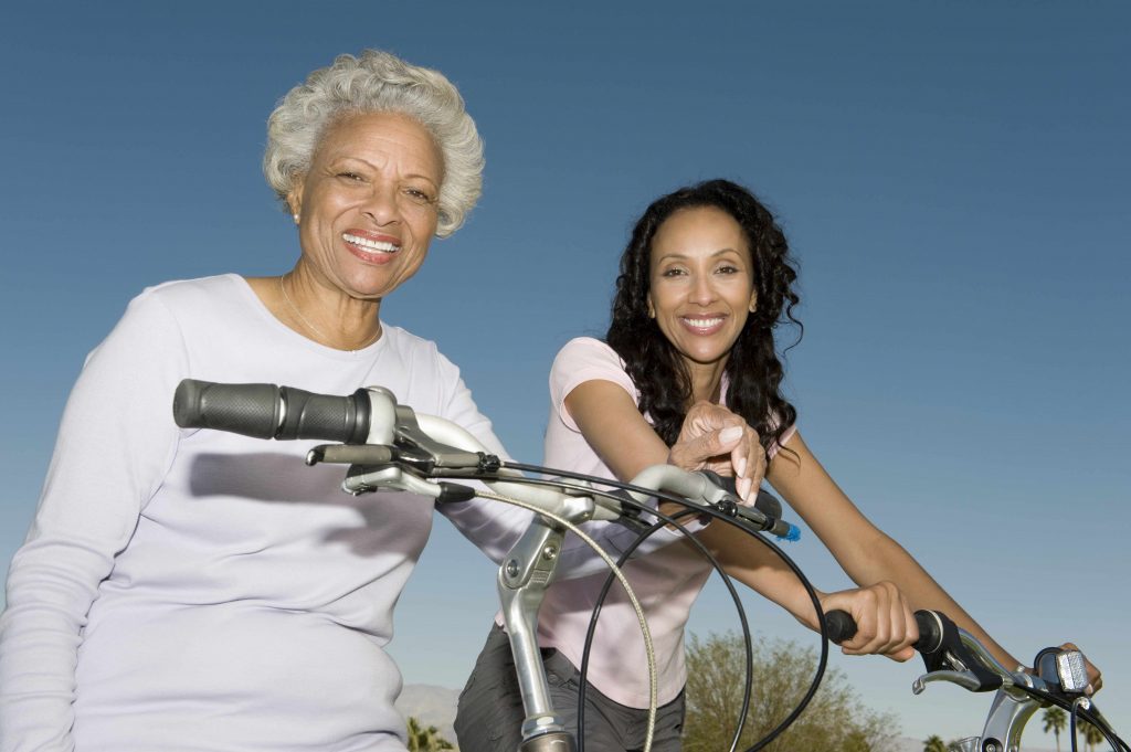 an African American mother and daughter sitting on bicycle against blue sky and smiling