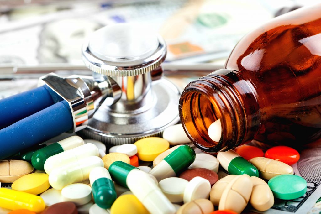 a pill bottle spilling prescription medicine, antibiotics, with a stethoscope nearby