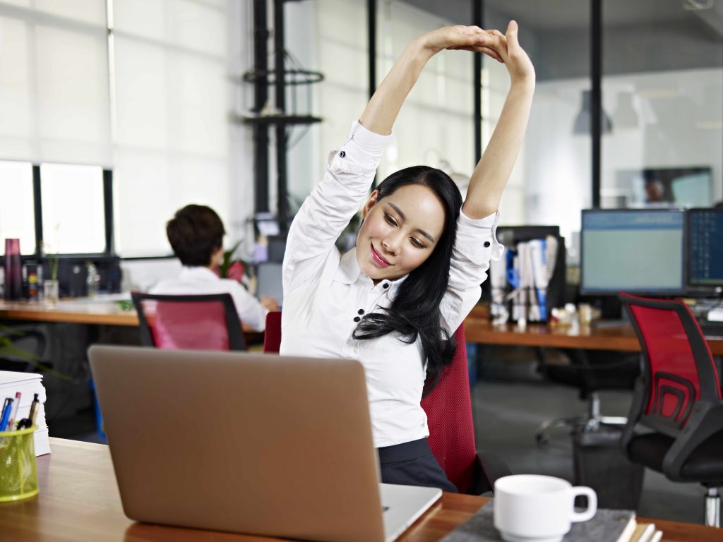 a young woman working in her office, stretching and exercising at her desk
