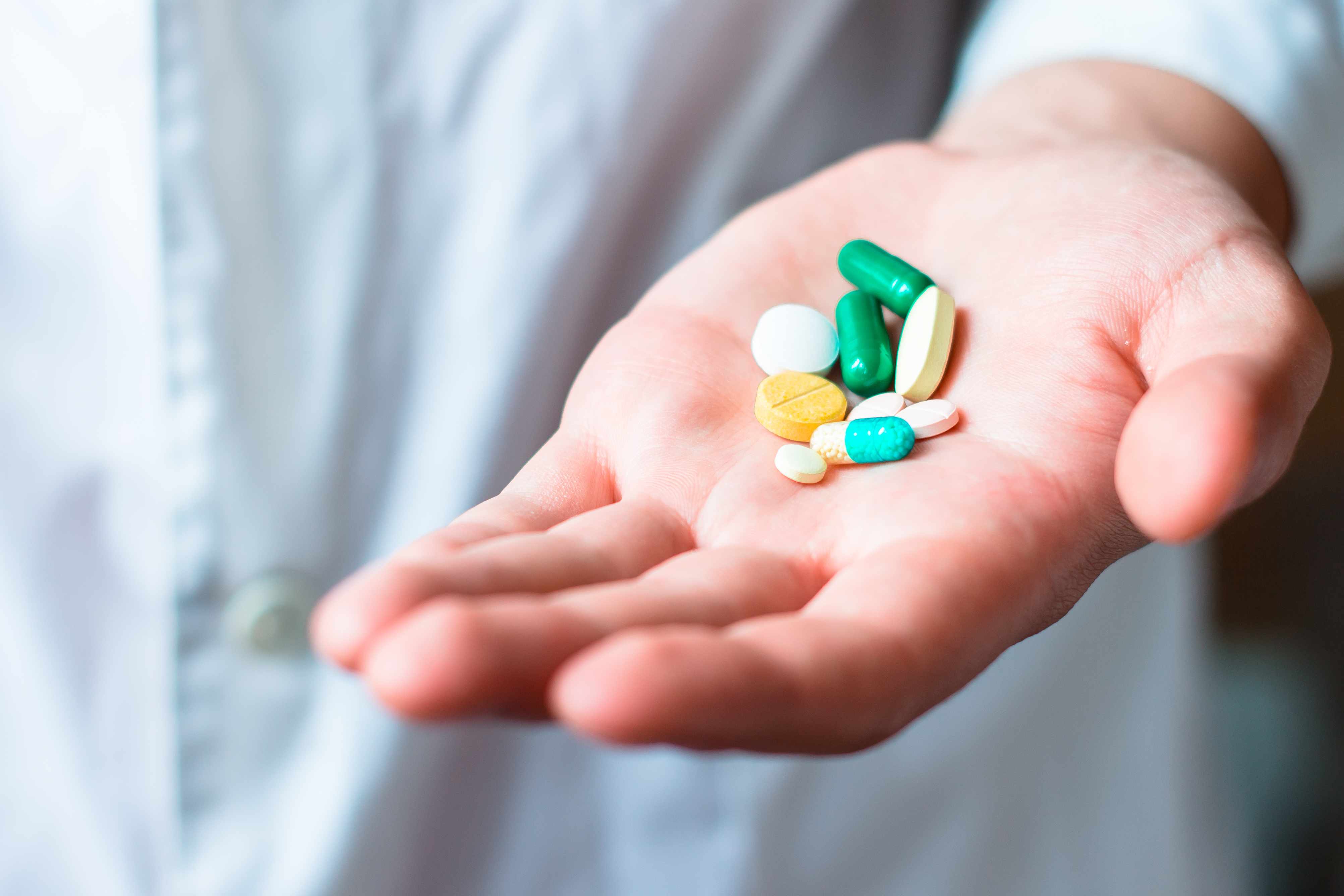 a person's hand full of medicine pills, prescription tablets, vitamins