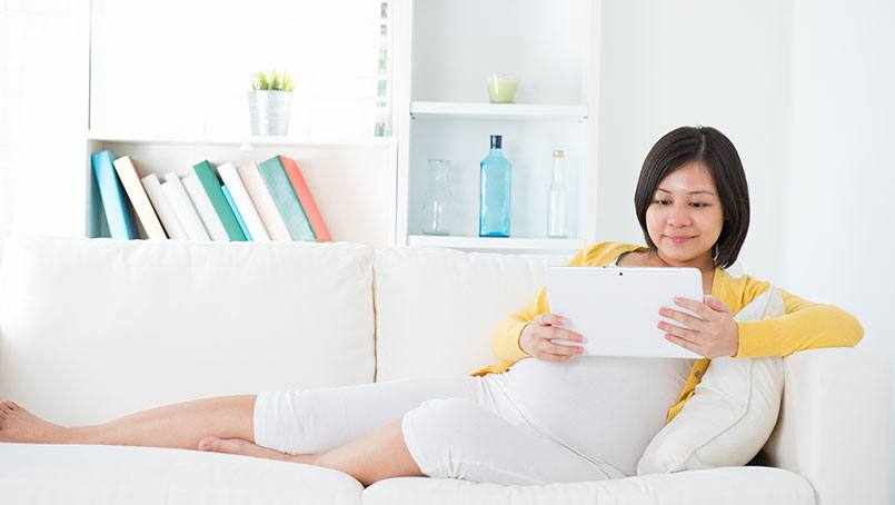 a pregnant woman sitting on a couch reading a book