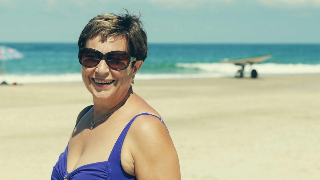 a middle-aged woman in bathing suit at the beach wearing sunglasses