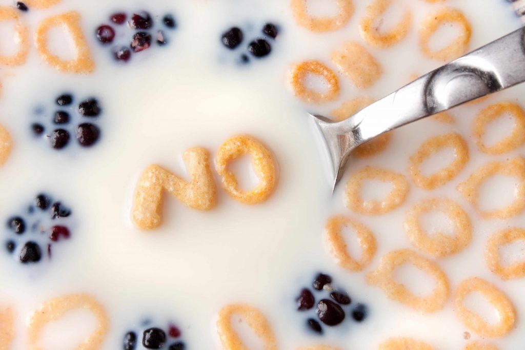 a close-up of a bowl of cereal and berries floating in milk, with cereal letters spelling out the word NO in a spoon