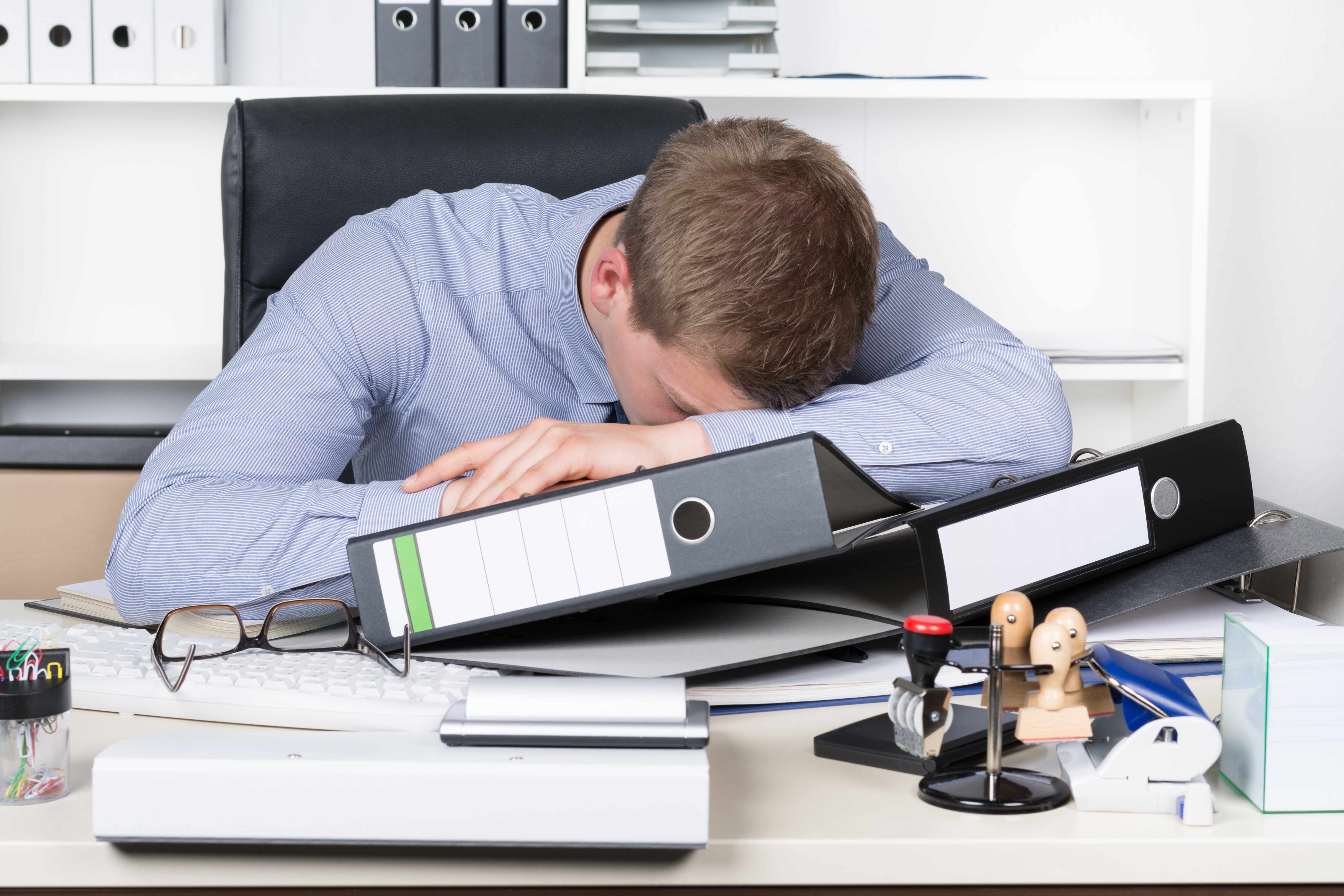 a businessman tired and resting on his desk with a pile of work (