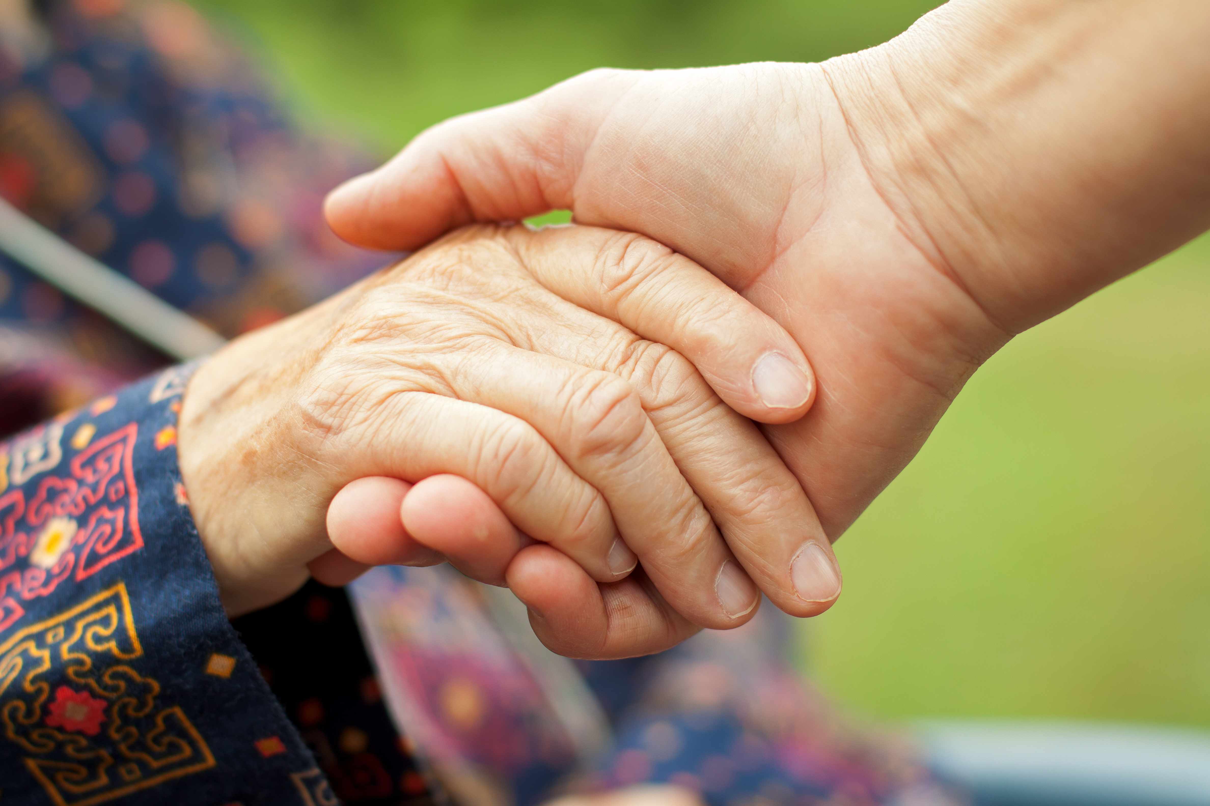 a caregiver holding the hand of an elderly person, senior citizen with arthritis, maybe Parkinson's disease