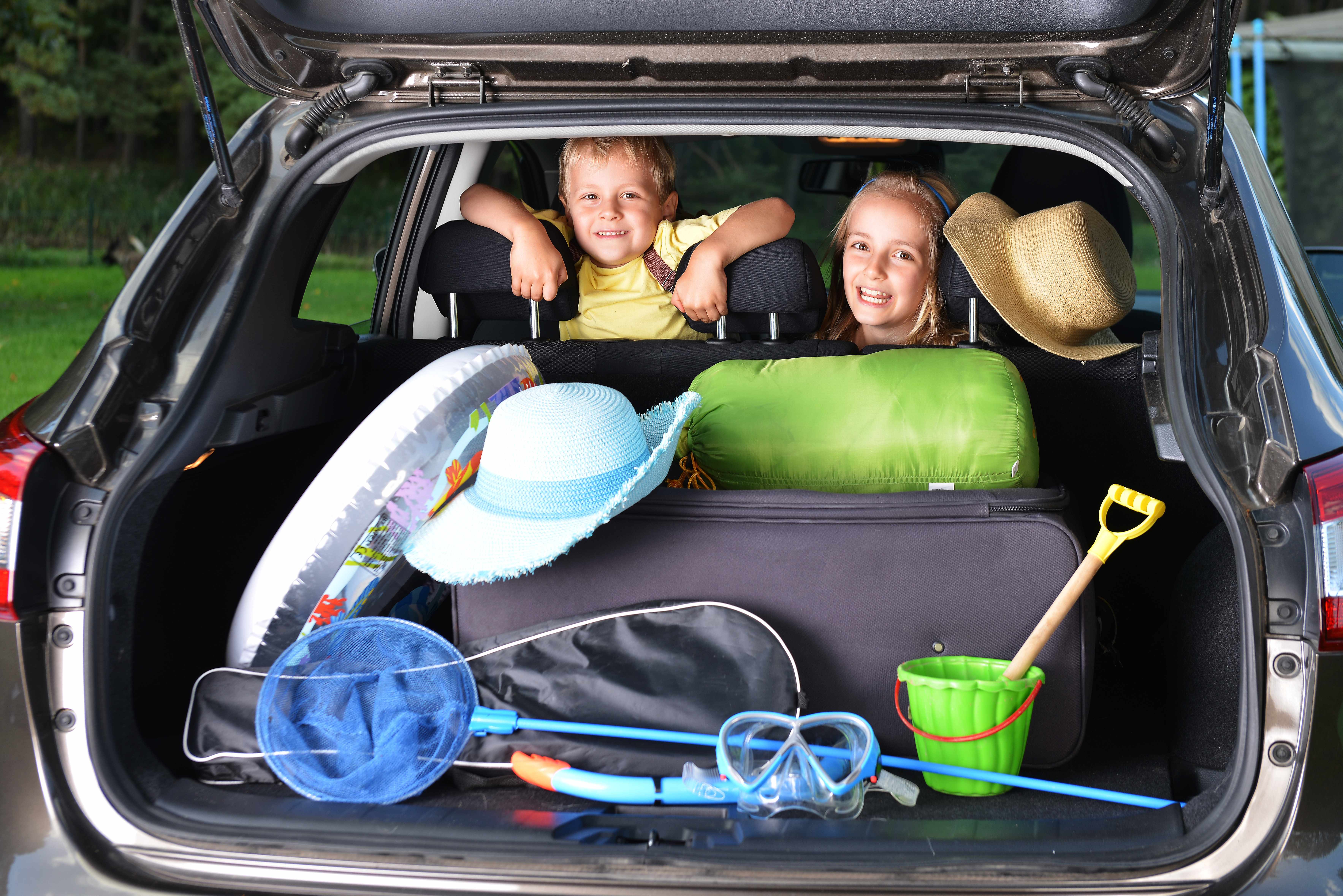 two children in a car with beach toys and vacation items packed in the back