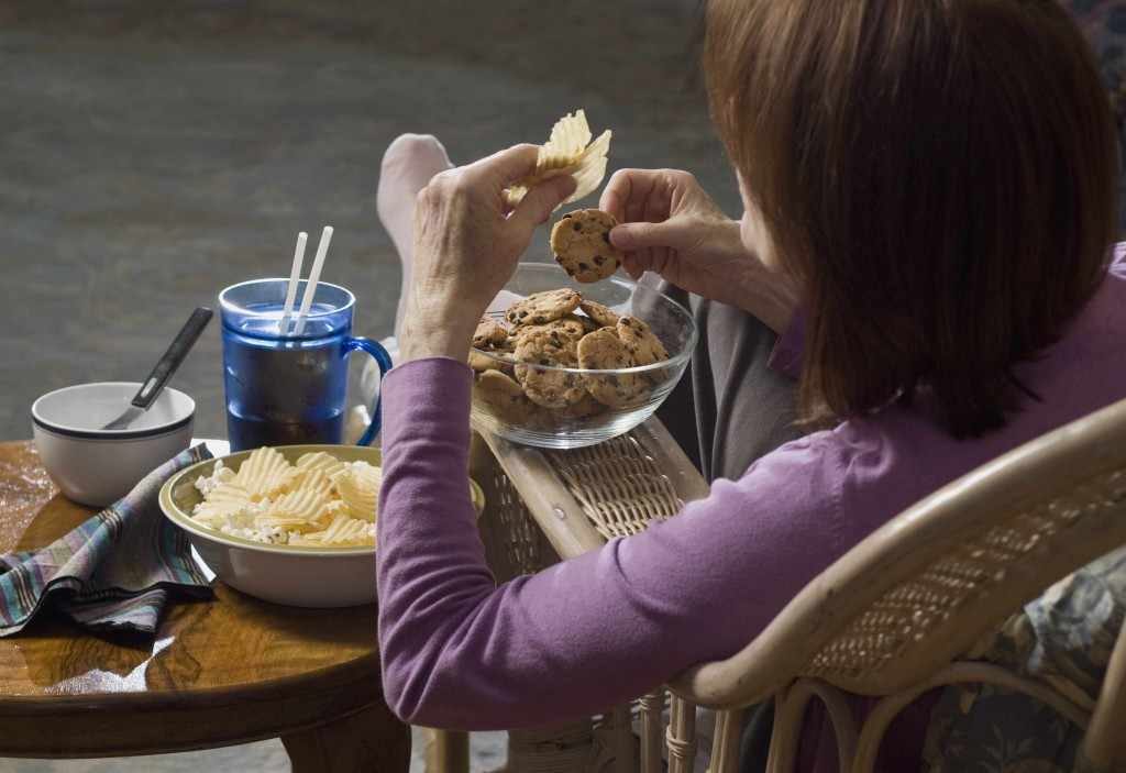 a woman seated, eating junk food, binge eating