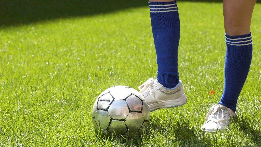 Pie y pierna junto al balón de fútbol; pie pateando pelota de futbol