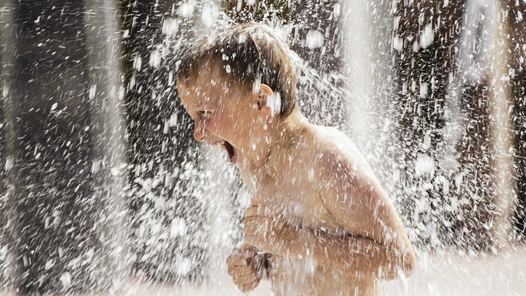 a young boy playing in a water fountain on a hot day with water spraying everywhere
