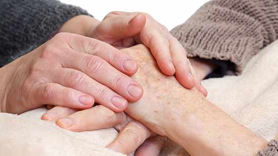 Un cuidador sostiene las manos de un paciente anciano