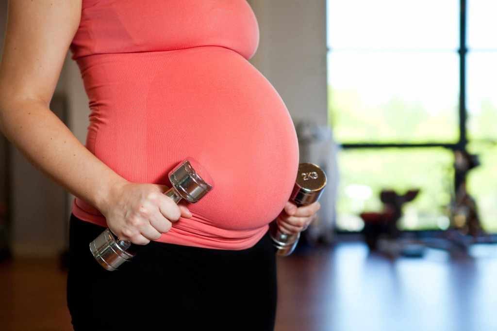 a pregnant woman is exercising and working out with dumbbell weights