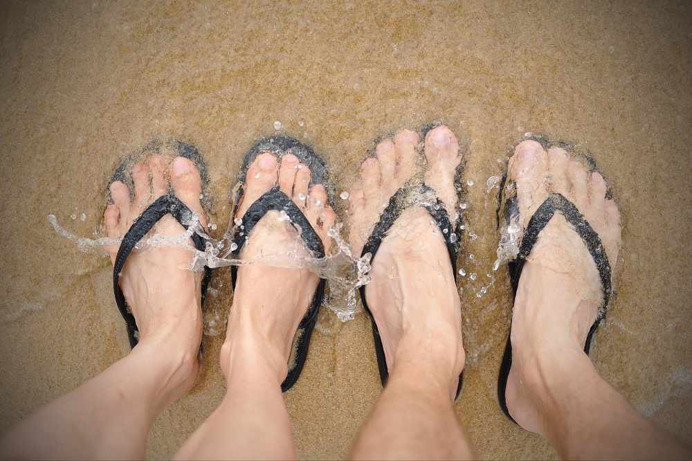 two people at the beach with flip flop sandals on their feet standing in sand with water covering their feet