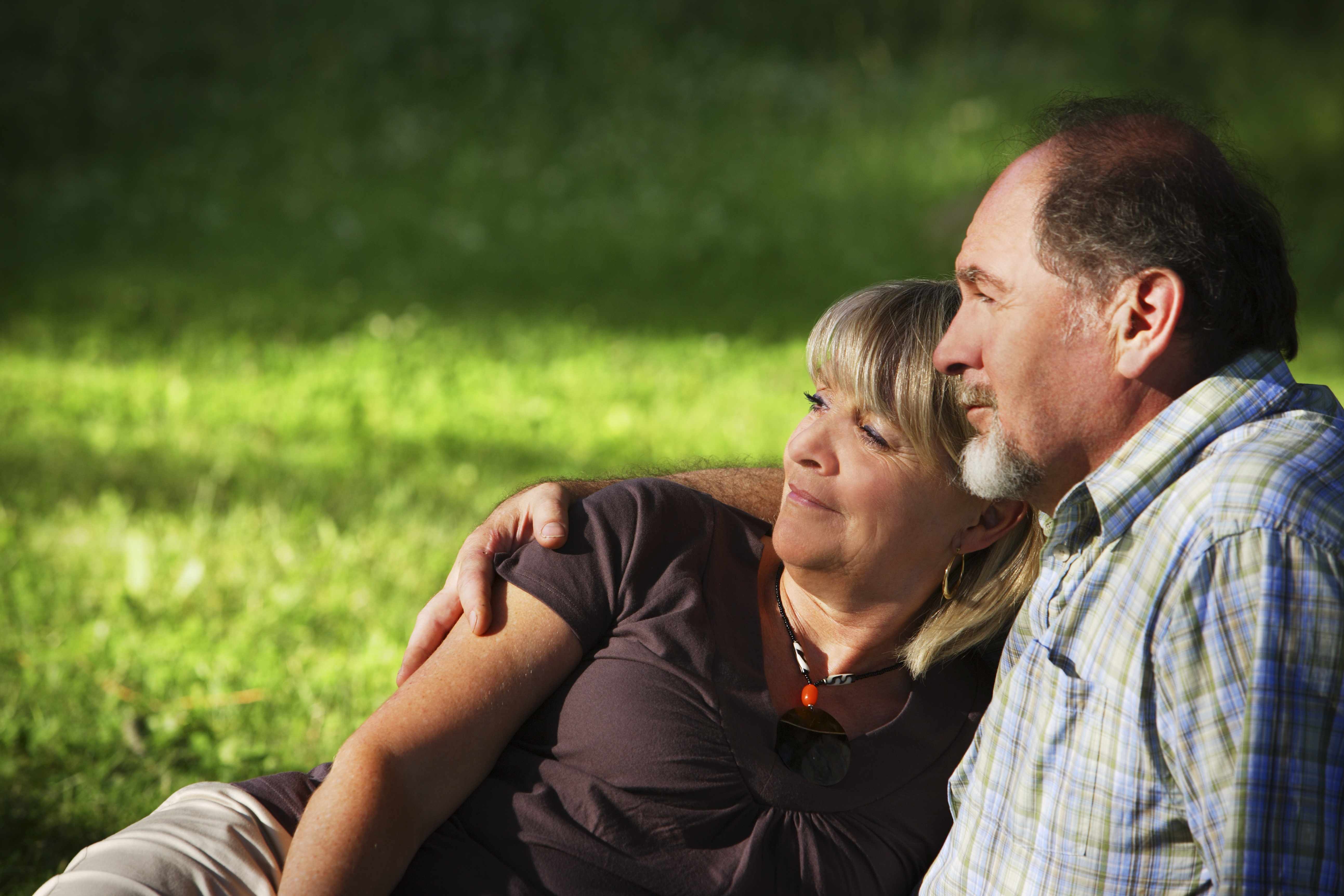 a middle-aged man and woman in each other's arms sitting outdoors in a park