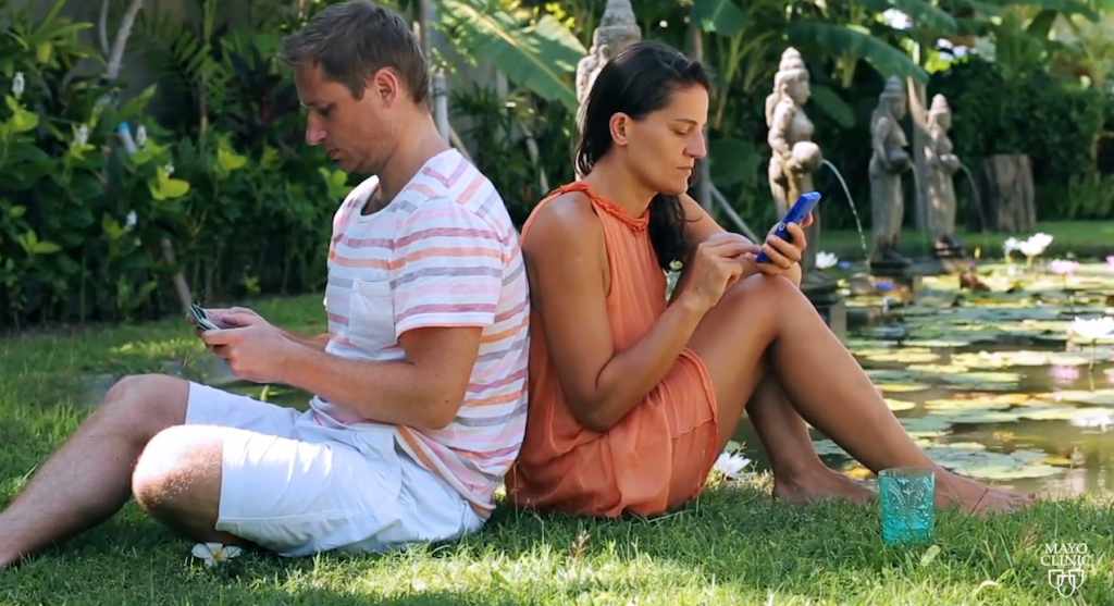 young couple sitting back to back on cell phones multitasking