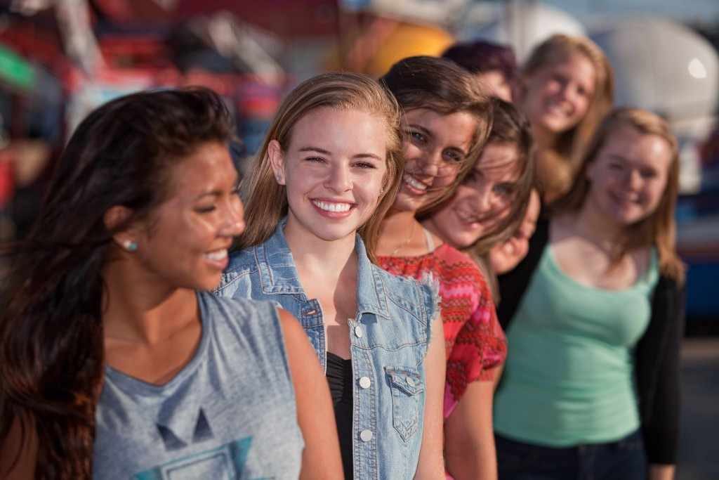 a group of healthy, smiling teenage girls standing in a row, one behind the other