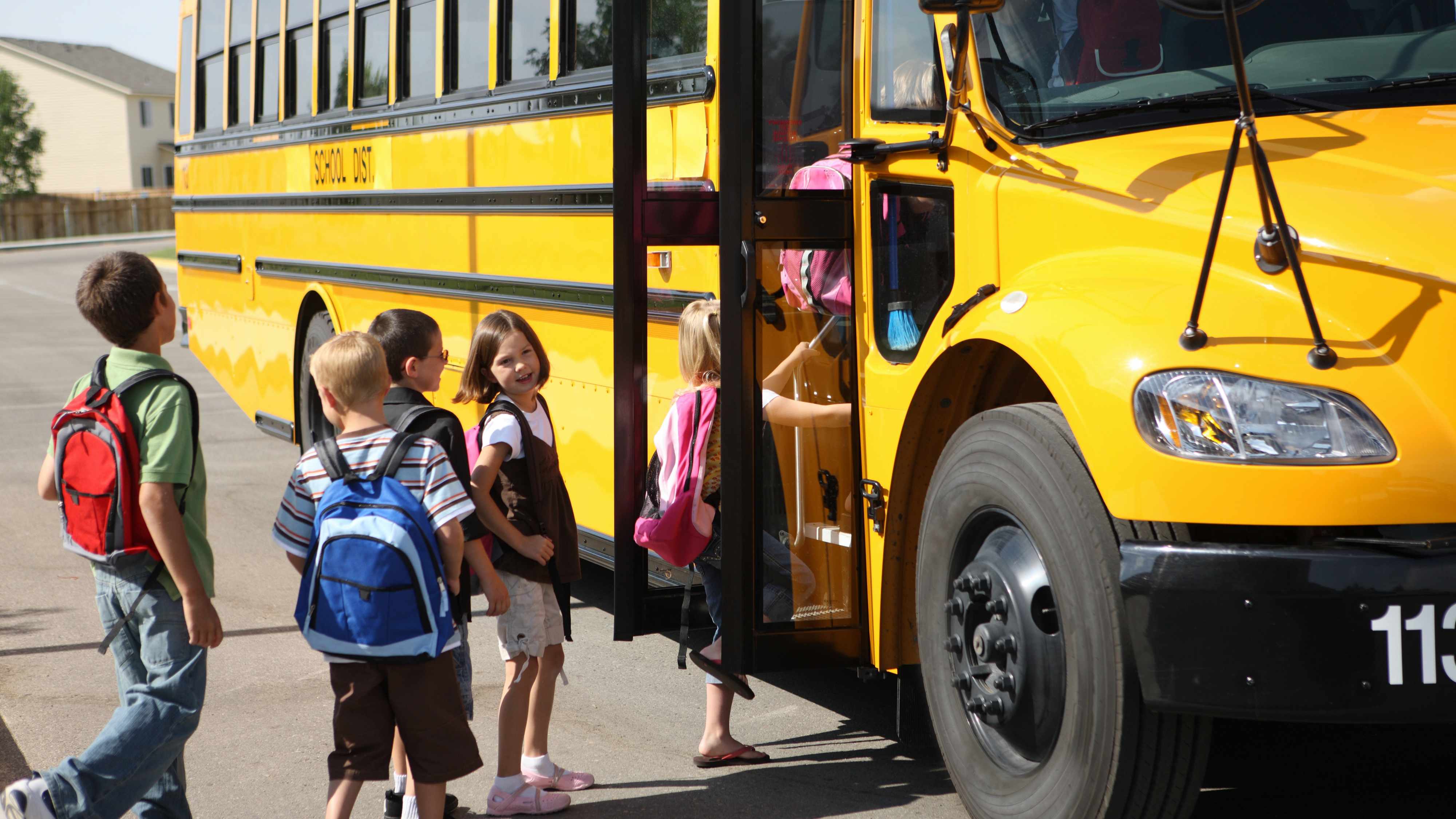 a group of young elementary school children with backpacks, getting on a school bus